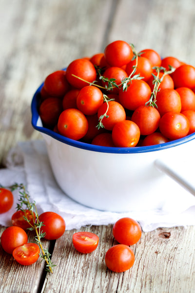 Mini tomatoes in a white bowl on a wooden table.