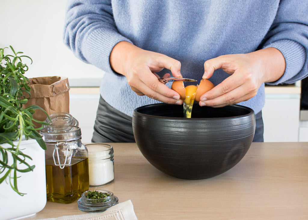 Woman adding eggs to a baking mixture.