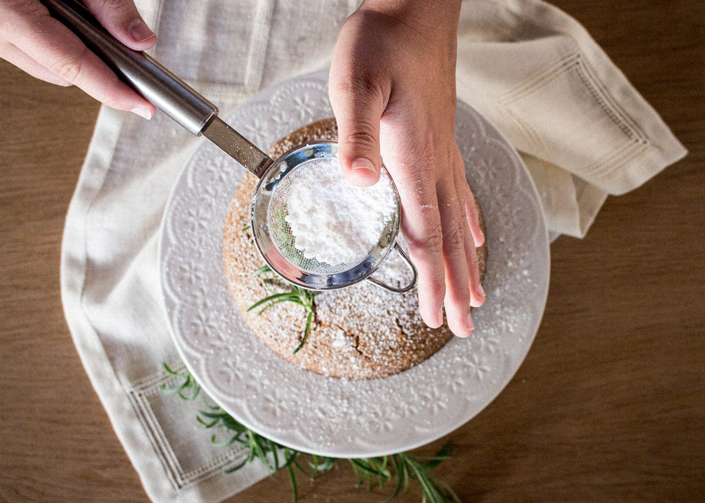 Woman decorating a cake with powdered sugar.