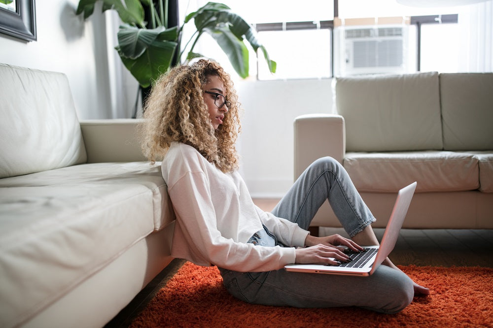 Lady sitting on the floor in a modern apartment using her laptop.